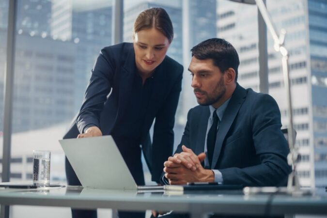 Successful Corporate CEO and Investment Manager Talking, Using Laptop Computer while Sitting in Meeting Room in Office. Two Successful Businesspeople Brainstorm on Prospective Fintech Investment Deal.
